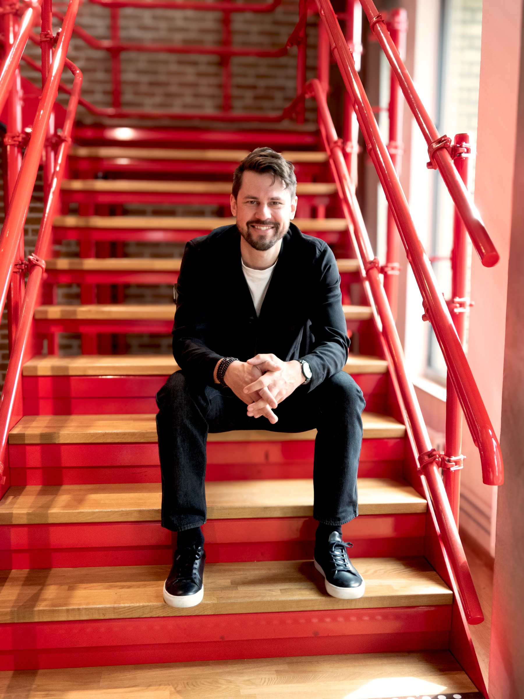 Adrian Swartz seated on the red staircase at More Alliance